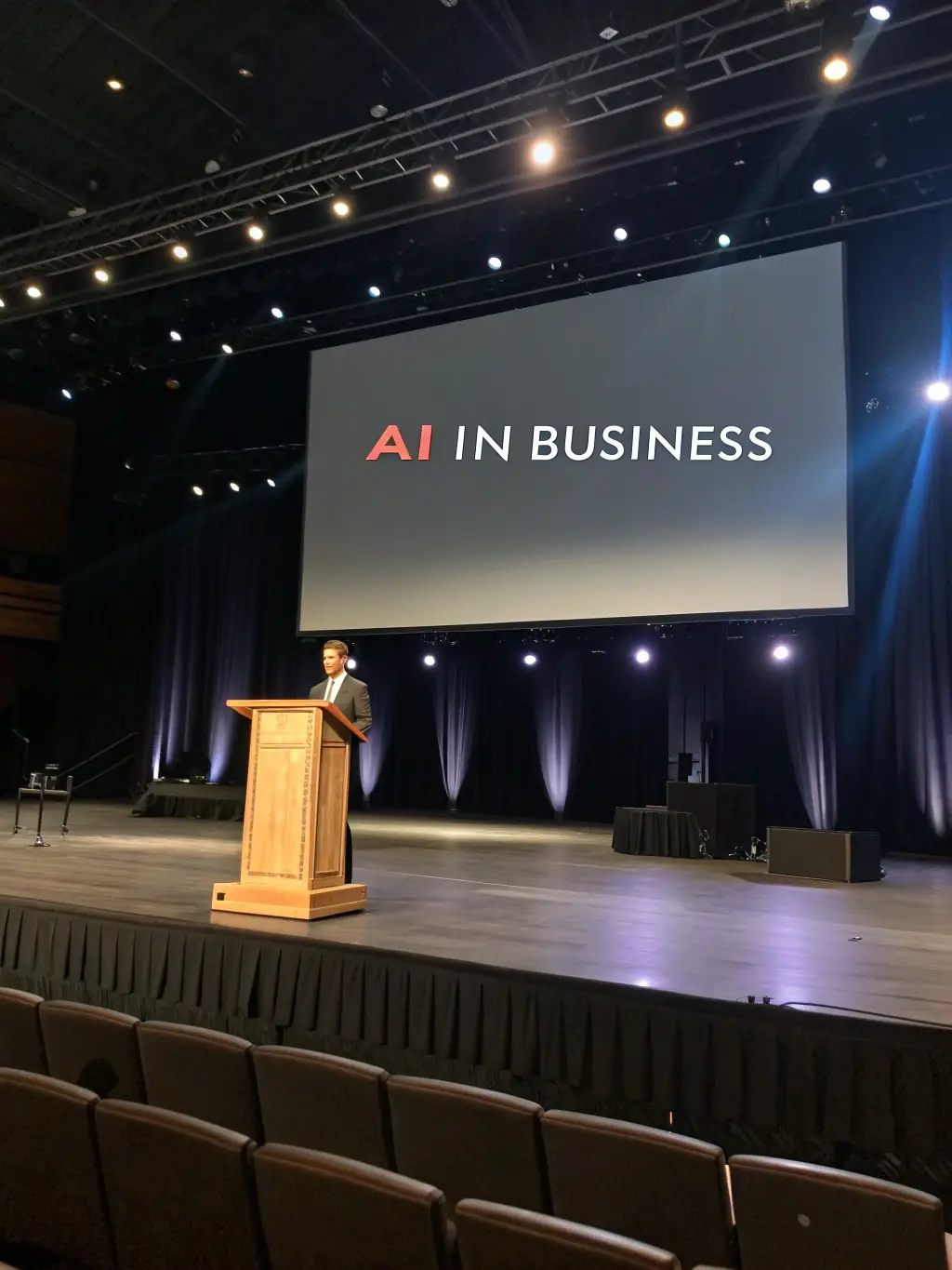 A photograph of a keynote speaker presenting on artificial intelligence at the Innovate UK conference, with engaged audience members in the foreground.